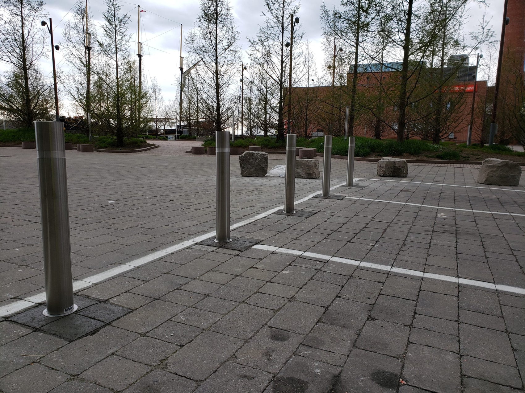 Three-step infographic showing a removable bollard workflow: closed position with post installed and locked in the ground sleeve, removed position with a worker lifting the post out of the sleeve, and safe/covered position with the hinged cover flipped down flat over the sleeve opening.