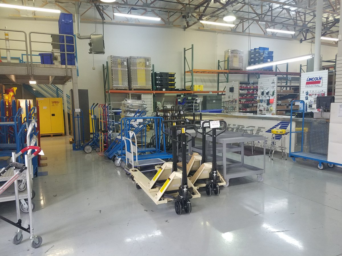 Warehouse interior with blue and beige industrial carts, pallet jacks, and material handling equipment neatly organized on a clean shop floor.